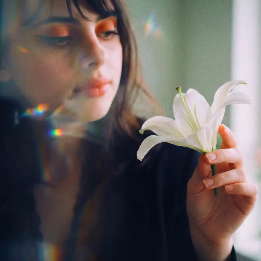 Lily looking at a white lily, prism light on her face