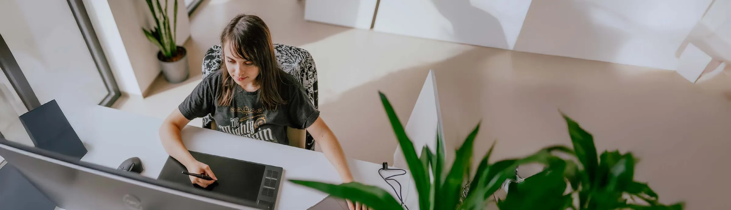 Lily drawing at her desk in a bright studio full of plants