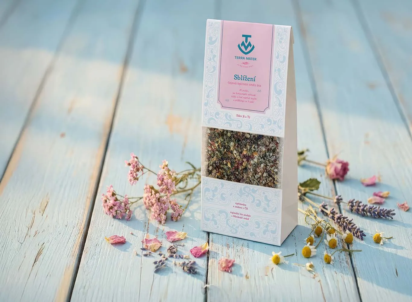 New pastel Terra Mater herbal tea pouch on a weathered wooden table with dried flowers